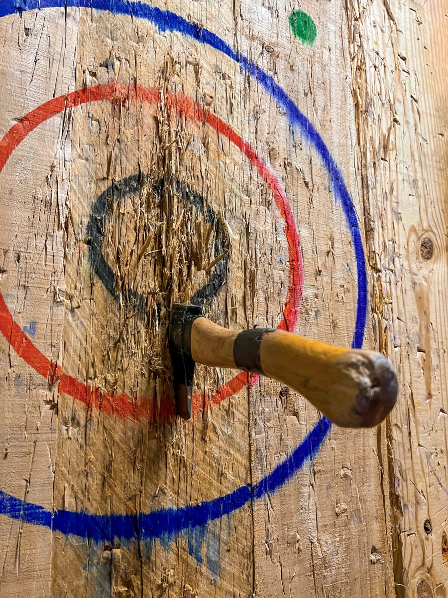 An axe embedded in a scarred wooden target board
